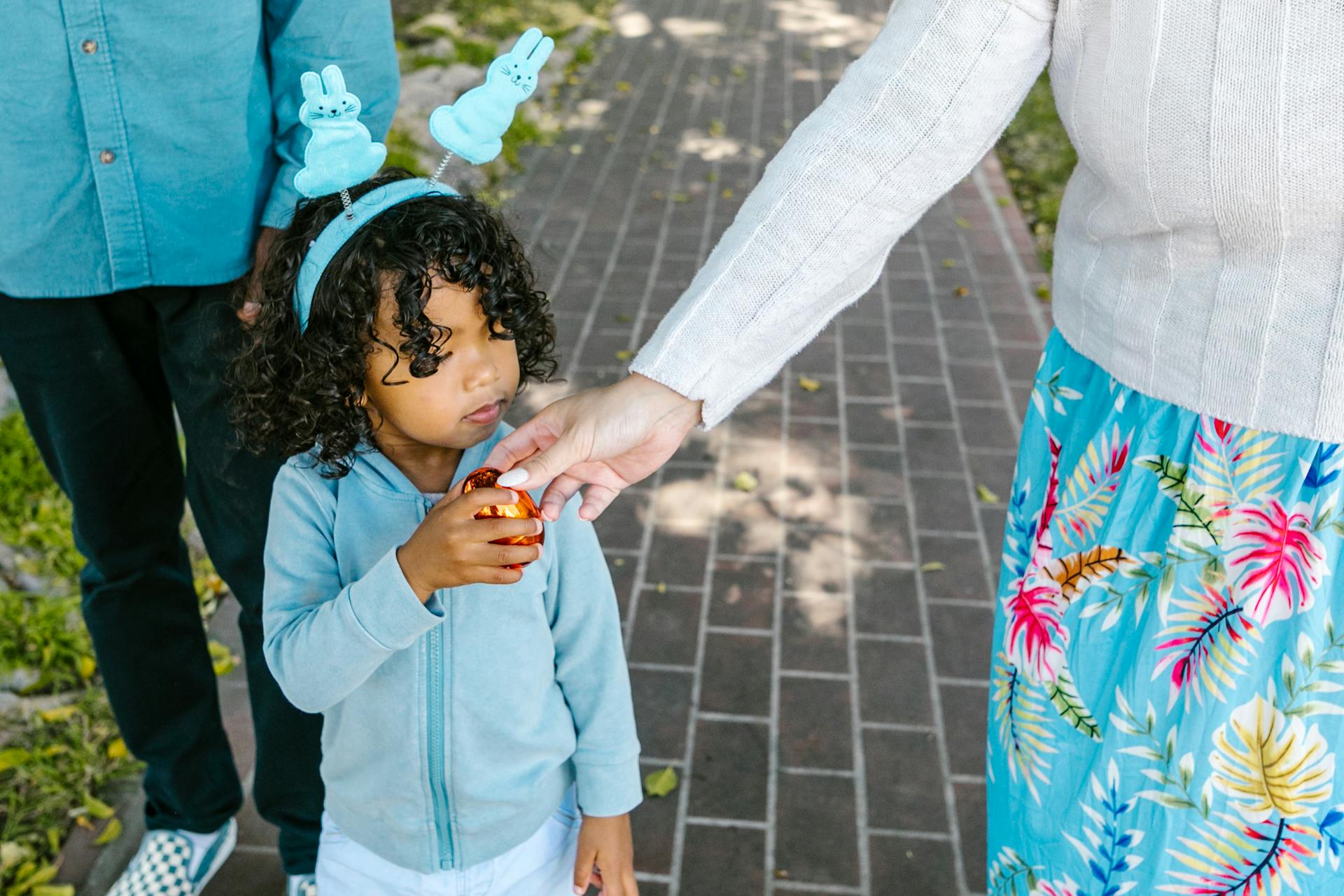 A young girl with bunny ears receives a festive Easter egg outdoors, celebrating Easter.