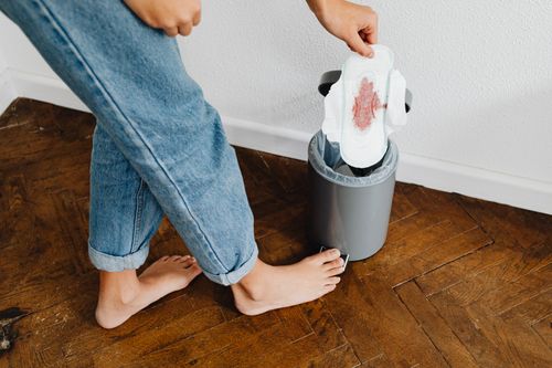Free A woman in blue jeans disposing of a used sanitary pad into a trash can indoors. Stock Photo