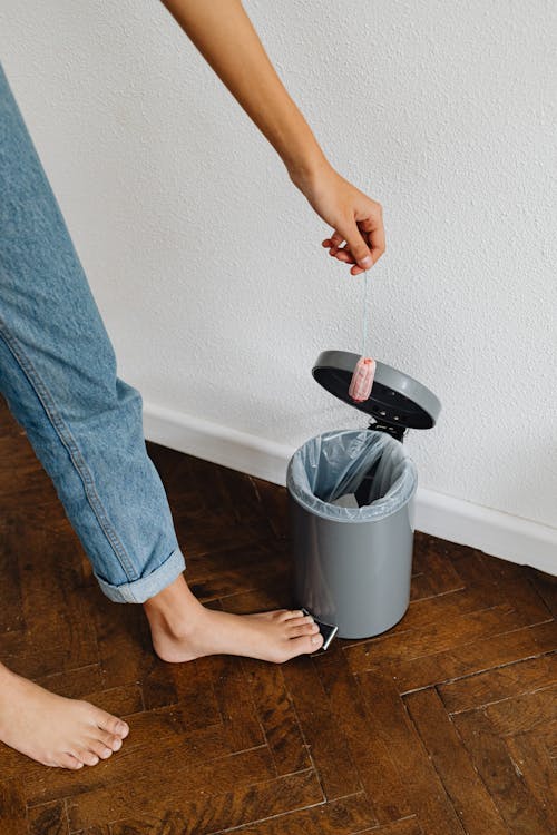 Free Person in Blue Denim Jeans Holding Black and White Plastic Trash Bin Stock Photo