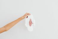 A hand holding a menstrual pad with blood stains, emphasizing menstruation awareness.