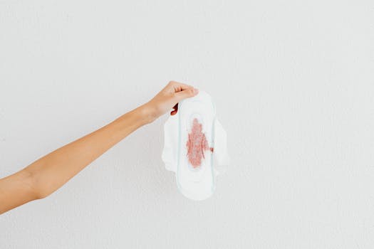 A hand holding a menstrual pad with blood stains, emphasizing menstruation awareness.
