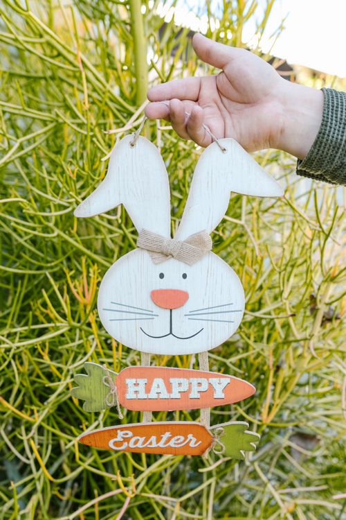 Free A cheerful Easter bunny decoration held by a hand amidst vibrant green foliage. Stock Photo