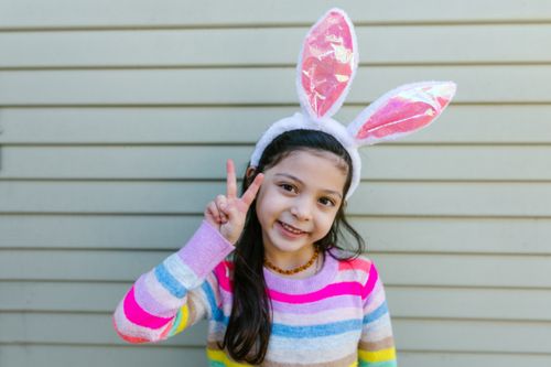 Free Cute girl with bunny ears headband and striped sweater making a peace sign outdoors. Stock Photo