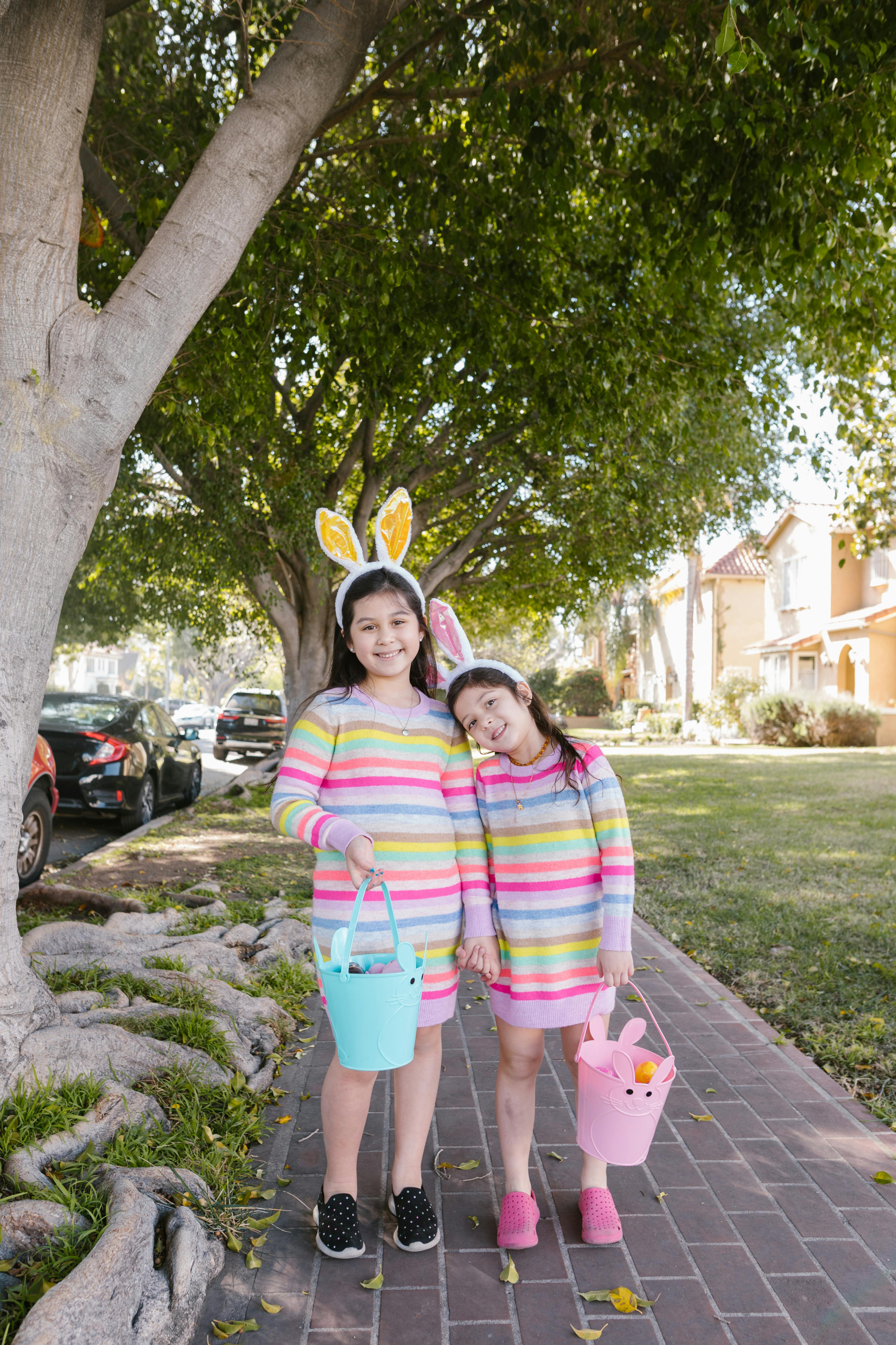 Two happy sisters in colorful outfits with bunny ears during a fun Easter egg hunt outdoors.