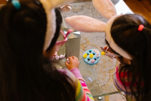 Free Two children with bunny ears enjoy playing with Easter toys at a glass table. Stock Photo