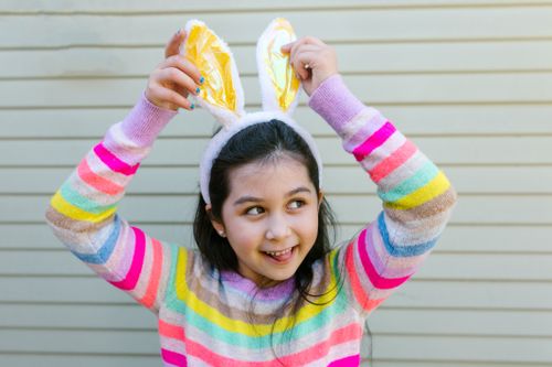 Free Smiling girl wearing bunny ears and colorful striped sweater, perfect for Easter themes. Stock Photo