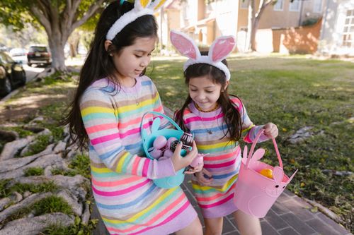 Free Two children in colorful dresses and bunny ears enjoy an Easter egg hunt outdoors. Stock Photo