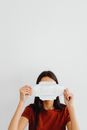 A woman holds a sanitary pad in front of her face against a minimalist background.