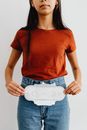 Young woman in casual outfit holding a sanitary pad against a white background.