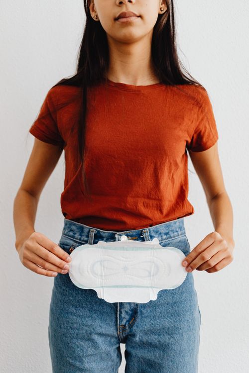 Free Young woman in casual outfit holding a sanitary pad against a white background. Stock Photo