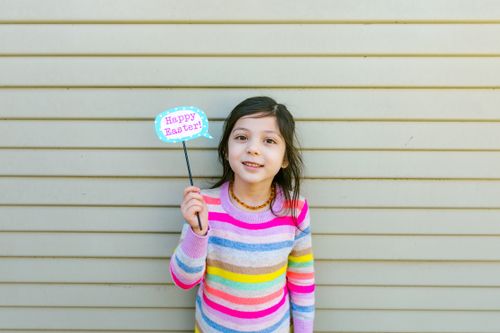 Free Cheerful girl with sign celebrating Easter in colorful striped sweater. Stock Photo