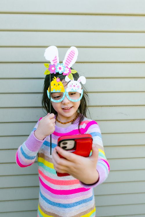 Free Happy child in colorful stripes taking a fun Easter selfie with bunny ear props. Stock Photo