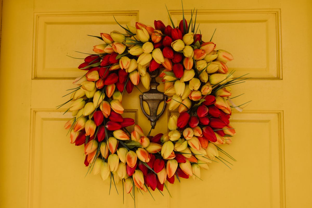 Vibrant red and yellow tulip wreath adorns a yellow front door, adding a festive touch. Stock Photo.