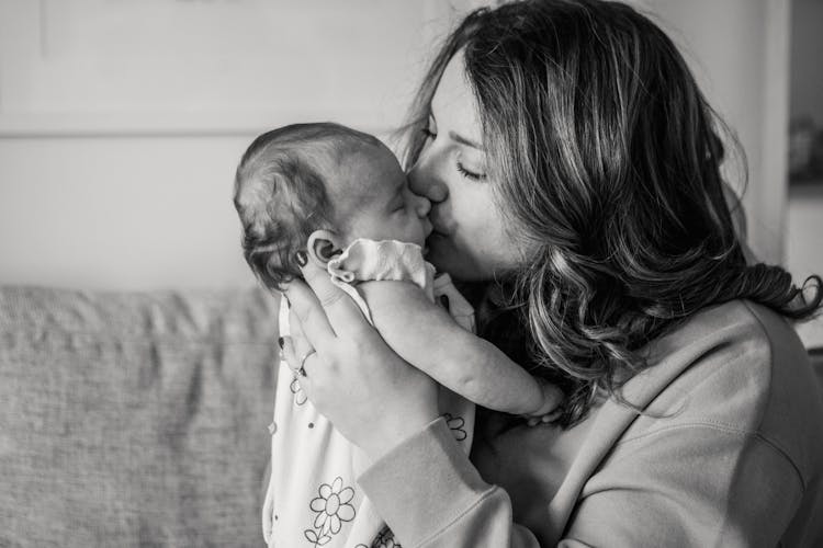 Grayscale Photo Of Woman Kissing A Baby