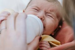 Close-up of a mother feeding her crying newborn with a bottle.