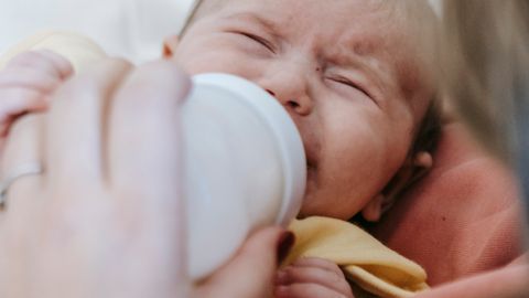Close-up of a mother feeding her crying newborn with a bottle.