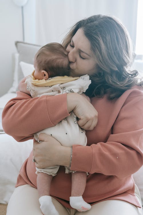 Free Mother kissing baby on bed Stock Photo