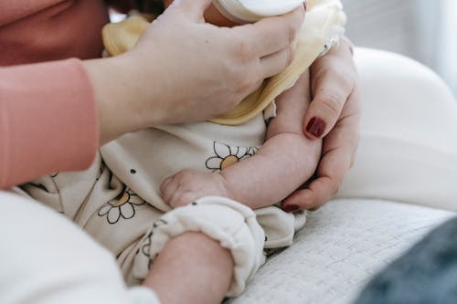Crop anonymous mother embracing and feeding adorable newborn baby with milk from bottle at home