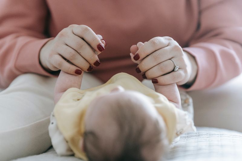 Mother holding her newborn baby's hands on a bed in soft daylight