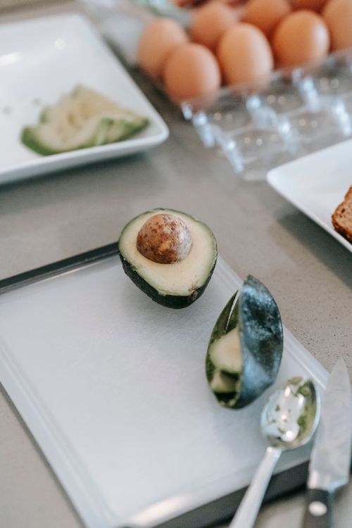 Free Halved avocado on a cutting board with eggs and food prep items in a kitchen setting. Stock Photo