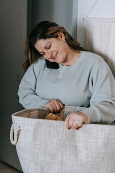 Happy woman multitasking with a smartphone while handling laundry indoors.