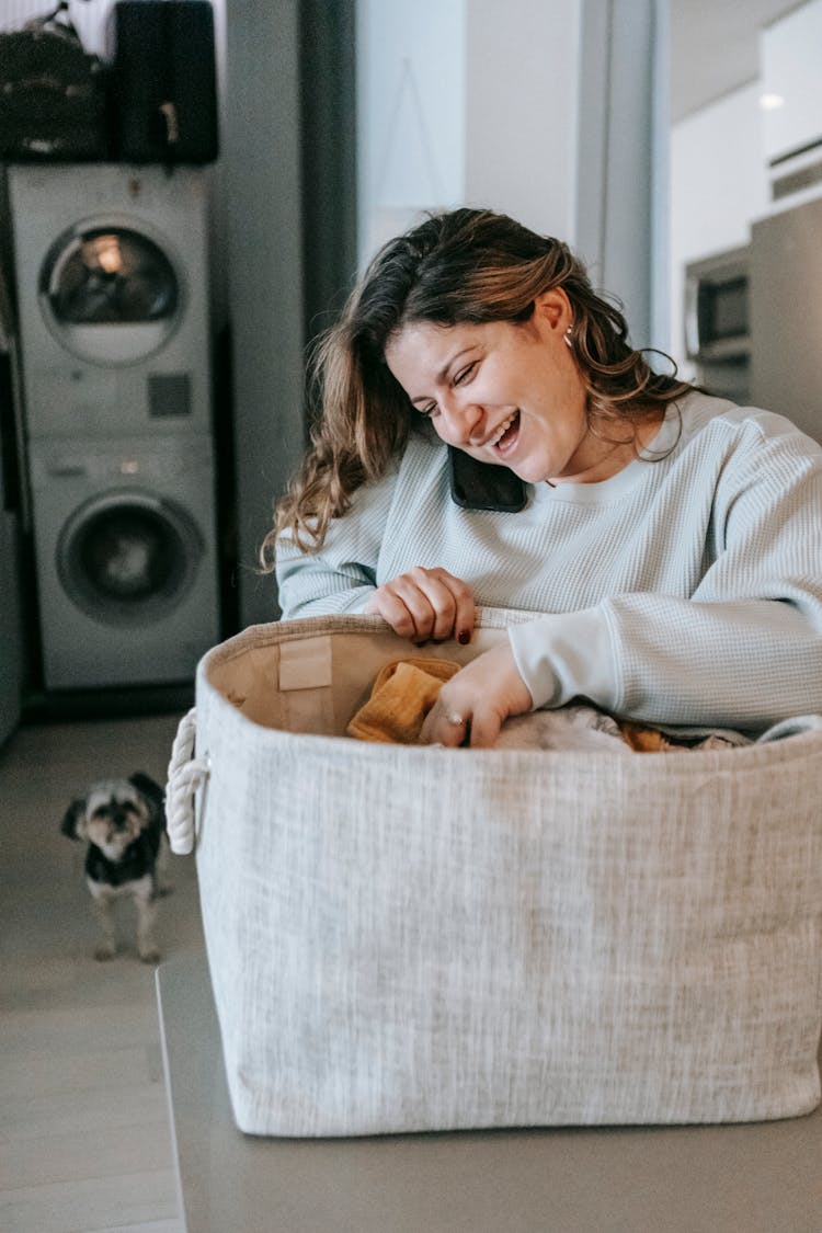 Happy Woman Unpacking Clean Clothes While Speaking On Smartphone