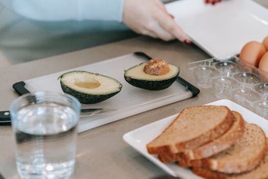 Sliced avocado and toast being prepared with eggs in a modern indoor kitchen.
