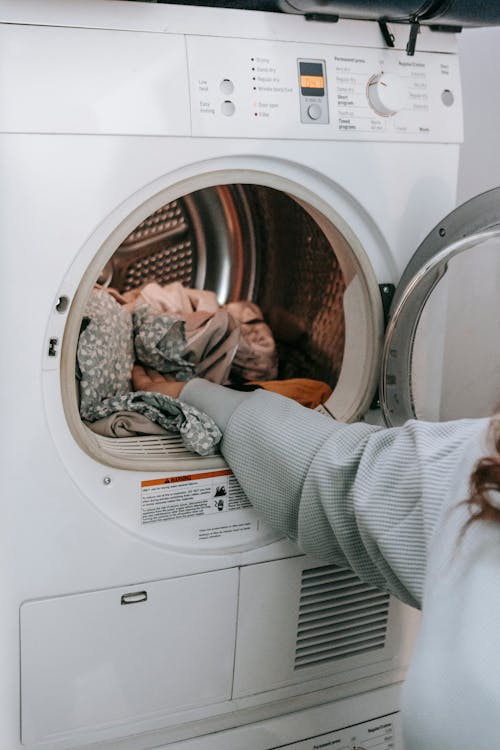 Free Crop unrecognizable female loading various dirty clothes in modern white washing machine during laundry routine in light room at home Stock Photo