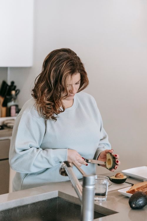 Free Focused female cook preparing avocado with knife while preparing toasts at counter with sink in kitchen during breakfast at home Stock Photo