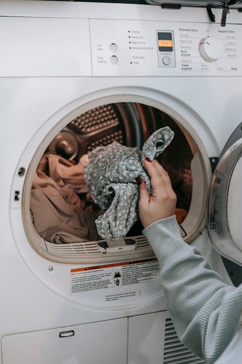 Free Crop unrecognizable female loading dirty clothes in modern white washing machine while doing housework routine in light room at home Stock Photo