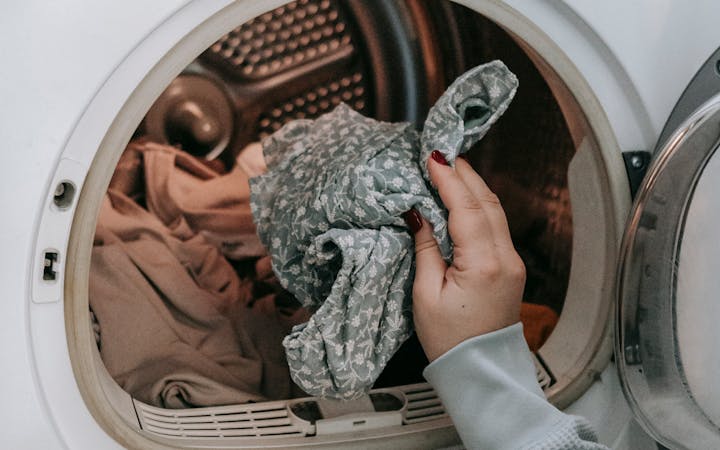 Crop unrecognizable female loading dirty clothes in modern white washing machine while doing housework routine in light room at home