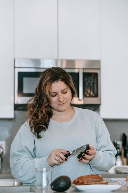 Free Optimistic female cook cutting ripe avocado while making toasts in modern light kitchen with microwave oven at home during breakfast Stock Photo