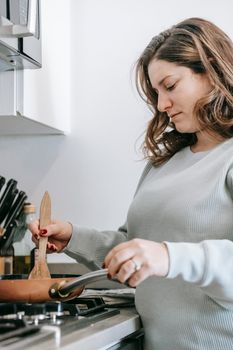 Side view of concentrated female cook stirring food in frying pan with wooden spatula while cooking on cooker in kitchen