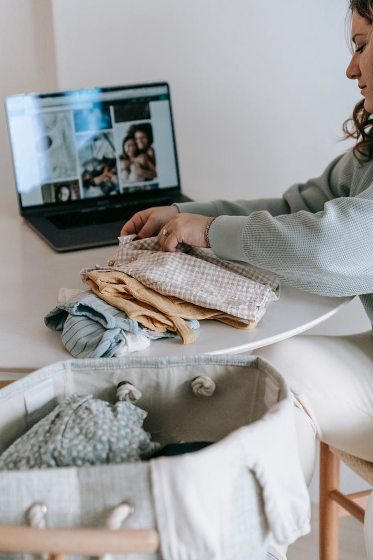 Woman Folding Baby Clothes Near Laptop