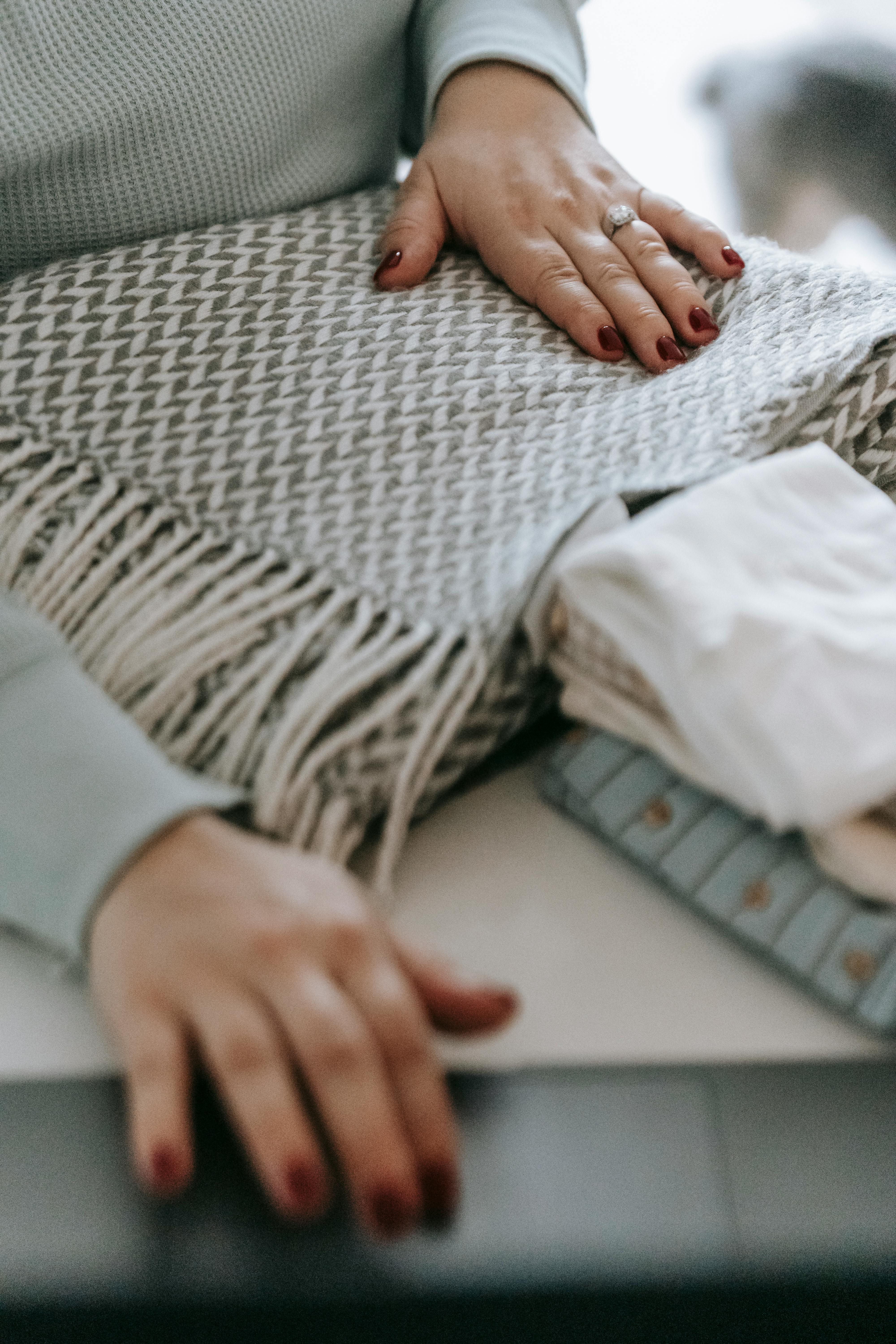 unrecognizable woman folding warm scarf near laptop