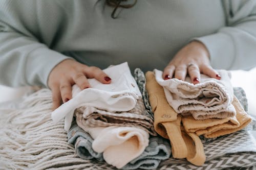 Free Crop faceless female with manicure arranging baby clothes on warm scarf while sitting at table in light room at home Stock Photo