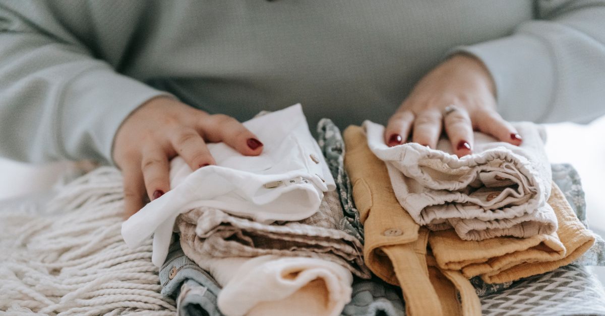 Separando as roupinhas do bebê Mãos de mulher organizando roupinhas de bebê sobre um tecido
