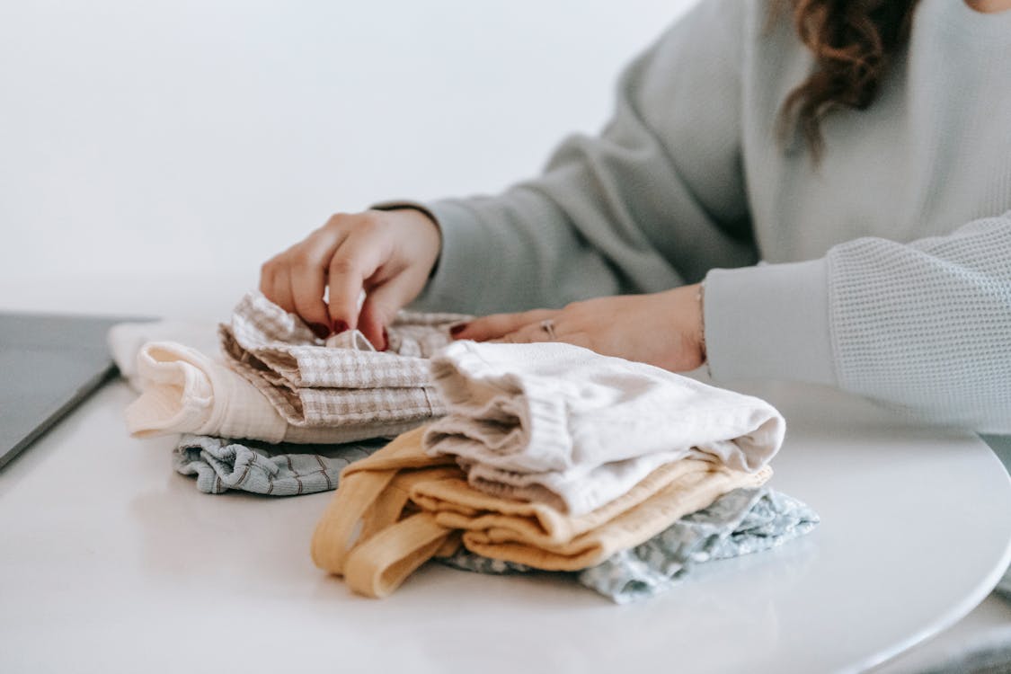 Free A woman organizing folded clothes on a table at home, emphasizing neatness and lifestyle. Stock Photo