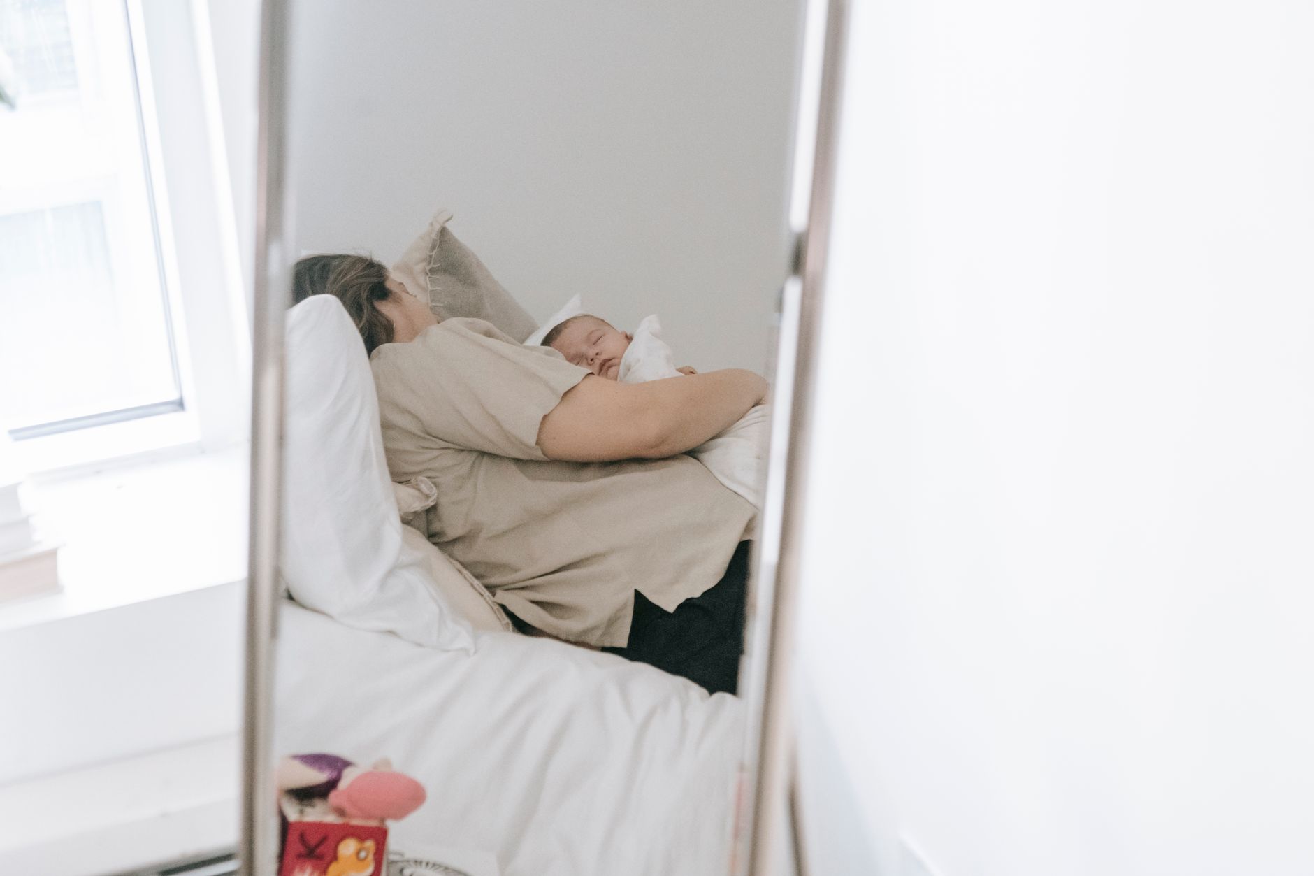 臥室窗邊放鏡子會更亮嗎?對睡眠有什麼影響 A serene moment of a mother holding her sleeping baby, reflected in a bedroom mirror.