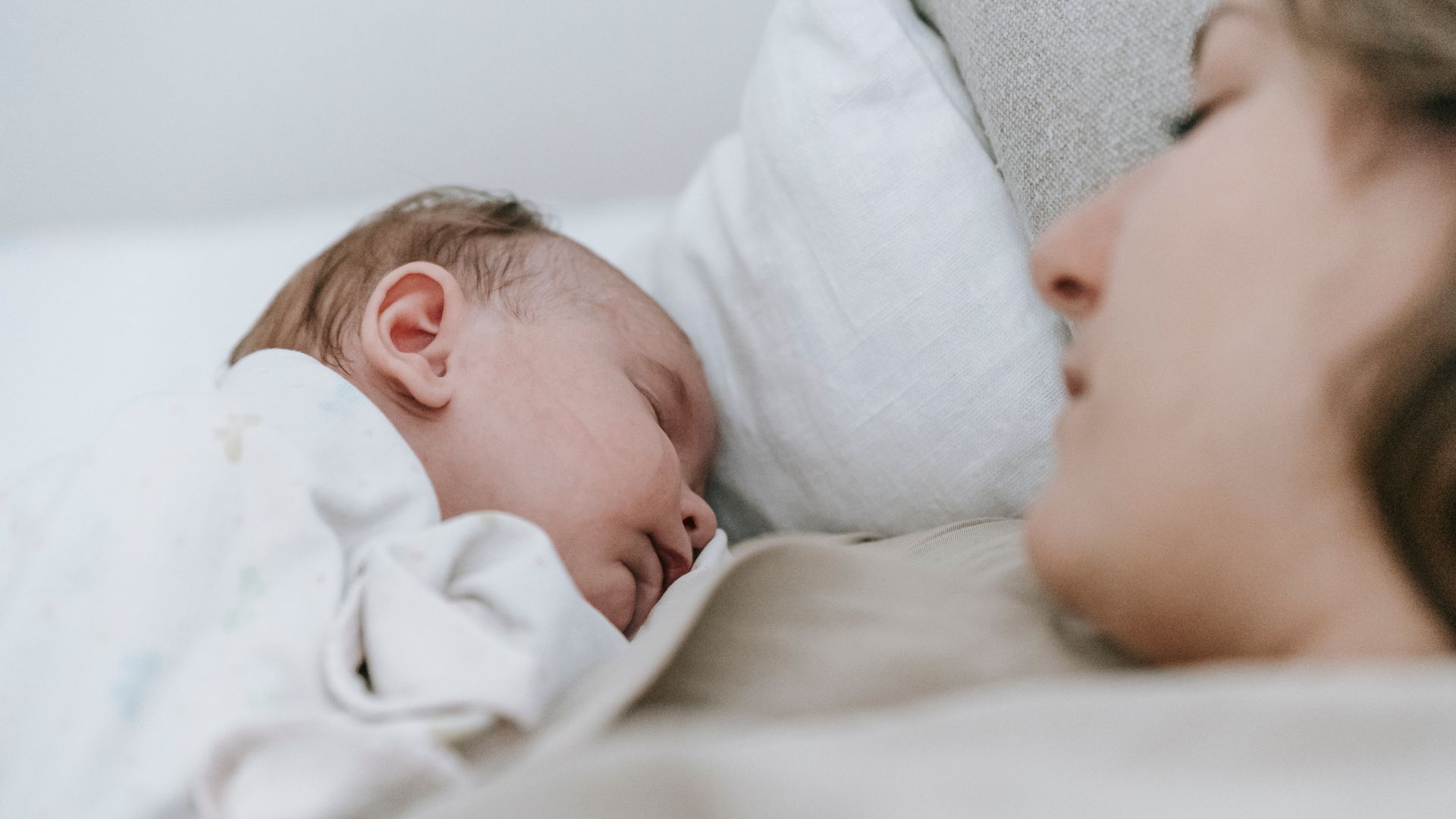 Modafinil for Postpartum Fatigue: An Effective Solution Side view of crop caring mother with cute infant baby sleeping peacefully together while lying on bed in light bedroom — modafinil for postpartum fatigue