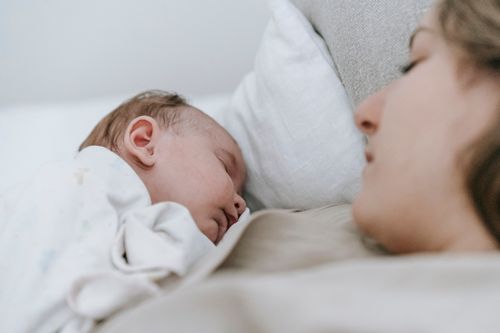 Free Side view of crop caring mother with cute infant baby sleeping peacefully together while lying on bed in light bedroom Stock Photo