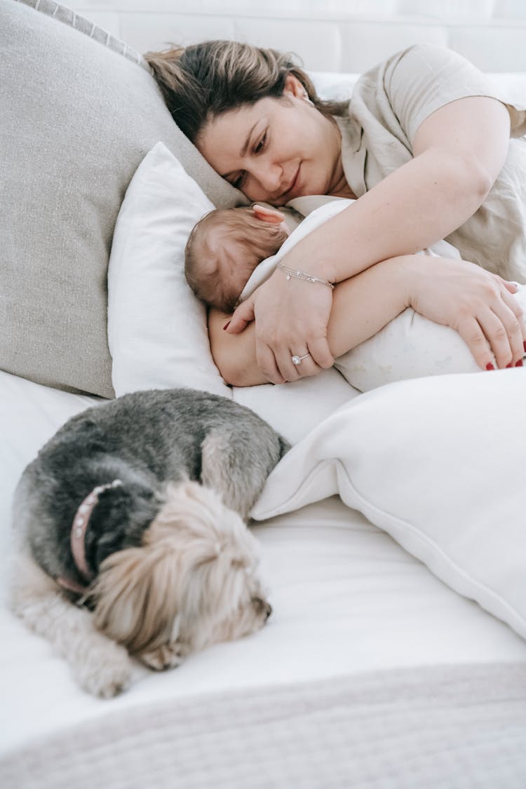 Mother Embracing Baby On Bed With Dog