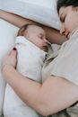 From above of caring mother embracing sleeping infant baby in swaddle while lying on comfortable bed in bedroom