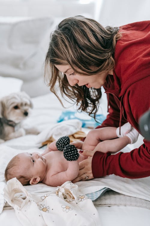 Side view of mother bending over newborn baby lying on comfortable couch near dog in light living room at home