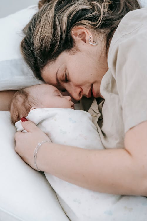 Mother with sleeping newborn baby on bed