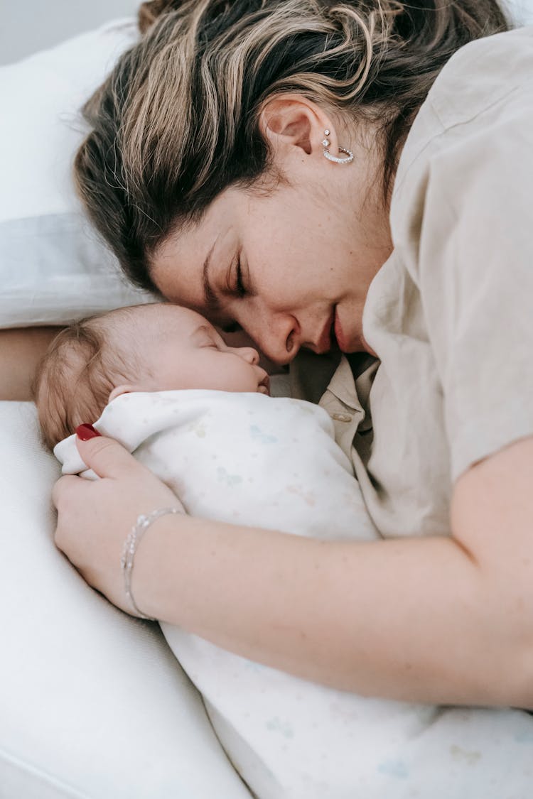 Mother With Sleeping Newborn Baby On Bed