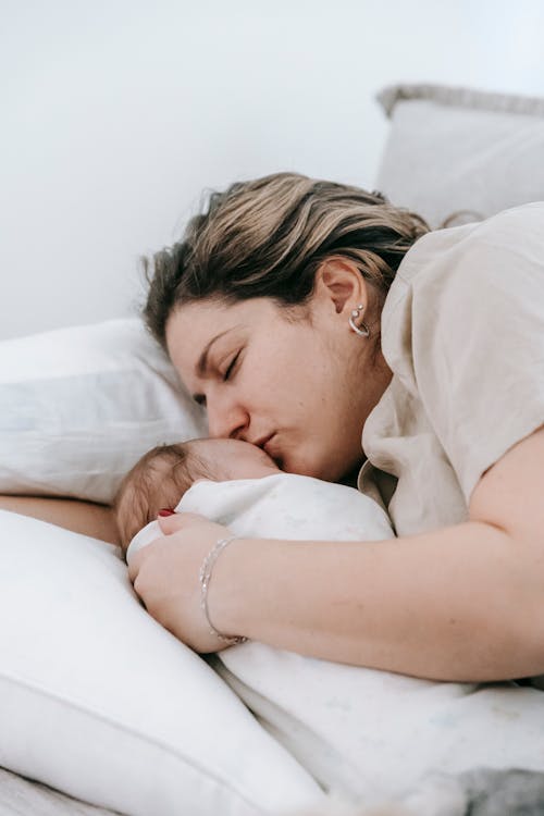 Caring mother kissing newborn baby on bed