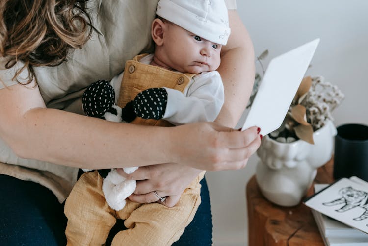 Faceless Mother Showing Picture To Infant Baby