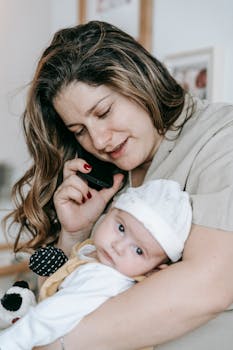 A mother lovingly holds her baby while talking on the phone, capturing a tender moment.