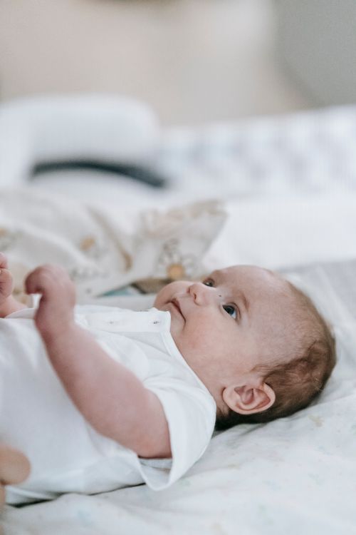 Free Adorable newborn baby in casual white clothes lying peacefully on comfortable bed in light room on blurred background at home Stock Photo